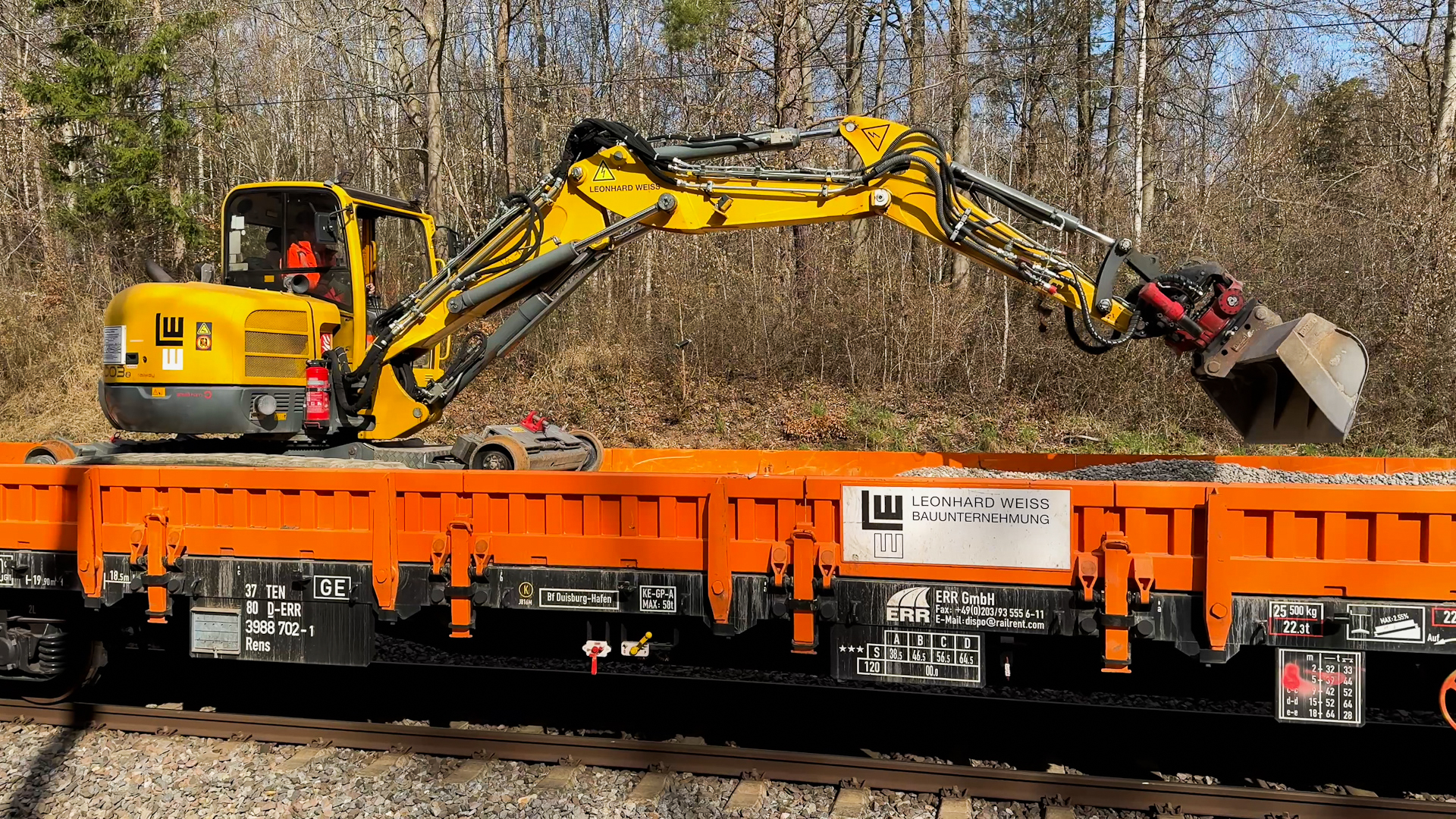 Zwei-Wege-Minibagger auf einem Arbeitszug bei Anfüllarbeiten mit Schottermaterial.