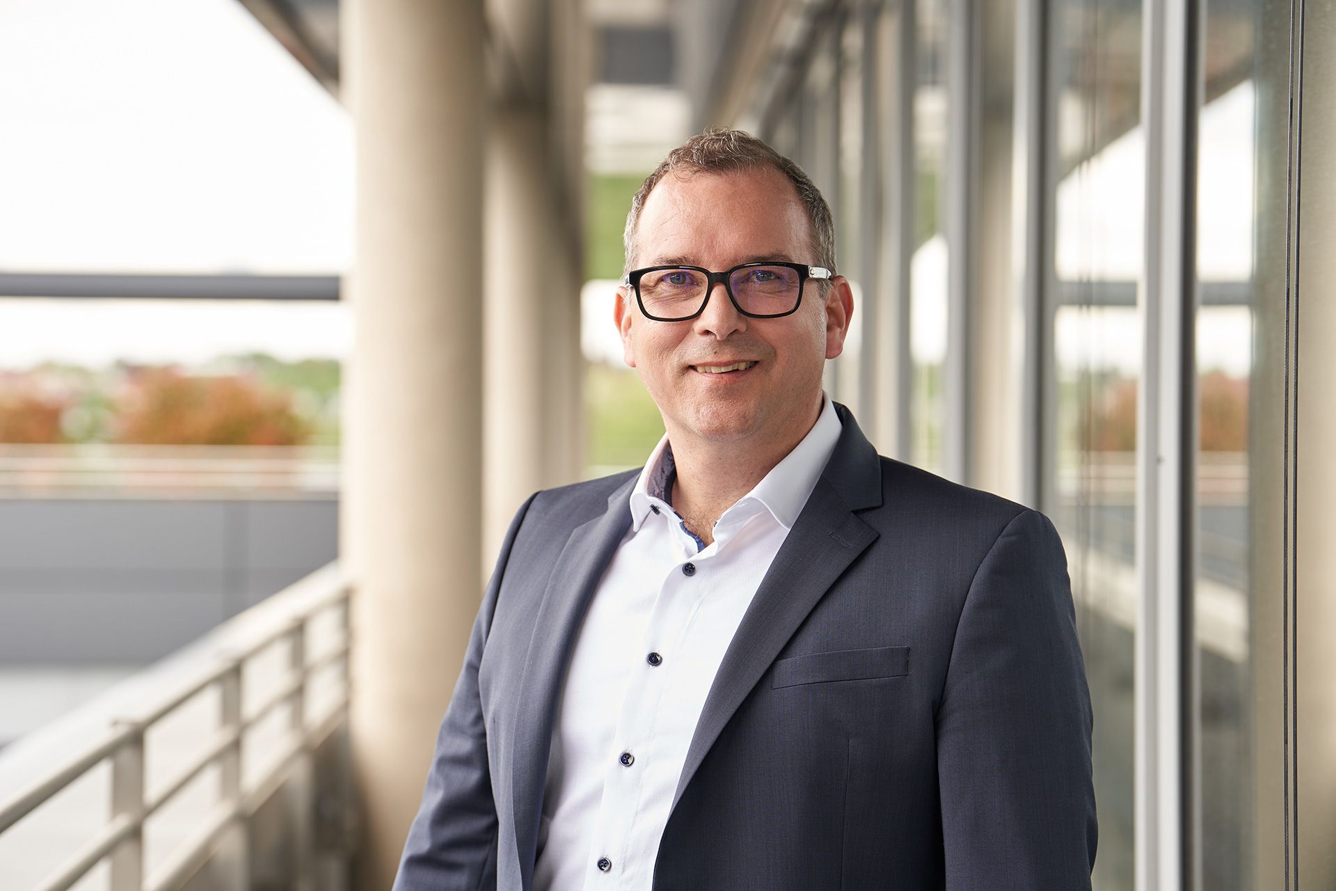 Christian Ott, der stv. Vorsitzender und Geschäftsführer Unternehmenssteuerung, in einem Anzug lächelnd vor großen Fenstern.
