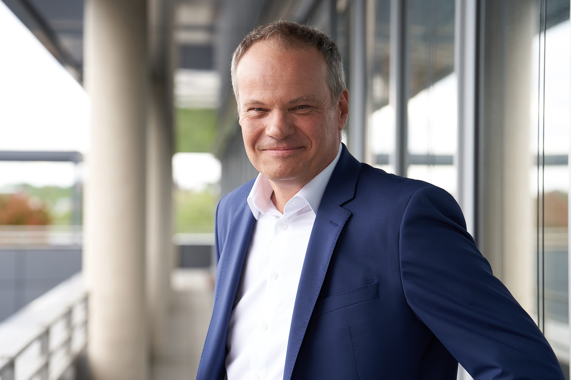 Christian Ott, der stv. Vorsitzender und Geschäftsführer Unternehmenssteuerung, in einem Anzug lächelnd vor großen Fenstern.