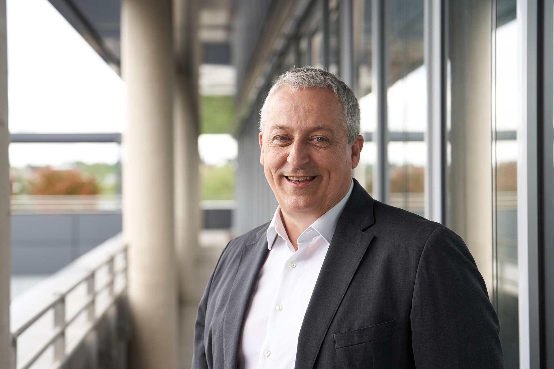 Ralf Schmidt, Gesellschafter und Geschäftsführer im Ressort Technik, lächelnd mit Anzug, im Außenbereich eines modernen Bürogebäudes stehend.