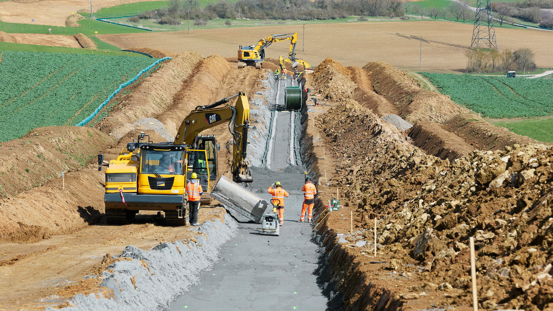 Eine Baustelle zeigt Bauarbeiter, die mit Baggern und anderen Maschinen an der Installation von Infrastruktur in ländlicher Umgebung arbeiten.