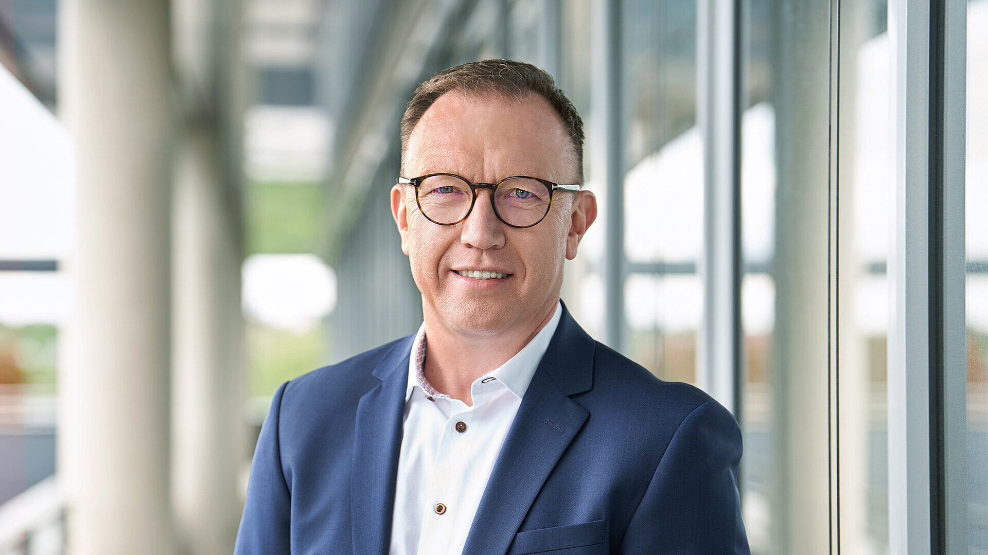 Foto von Marcus Herwarth, Leiter Geschäftsbereich Gleisinfrastrukturbau und Vorsitzender der Geschäftsführung, stehend in Anzug und Hemd vor einem modernen Bürogebäude.