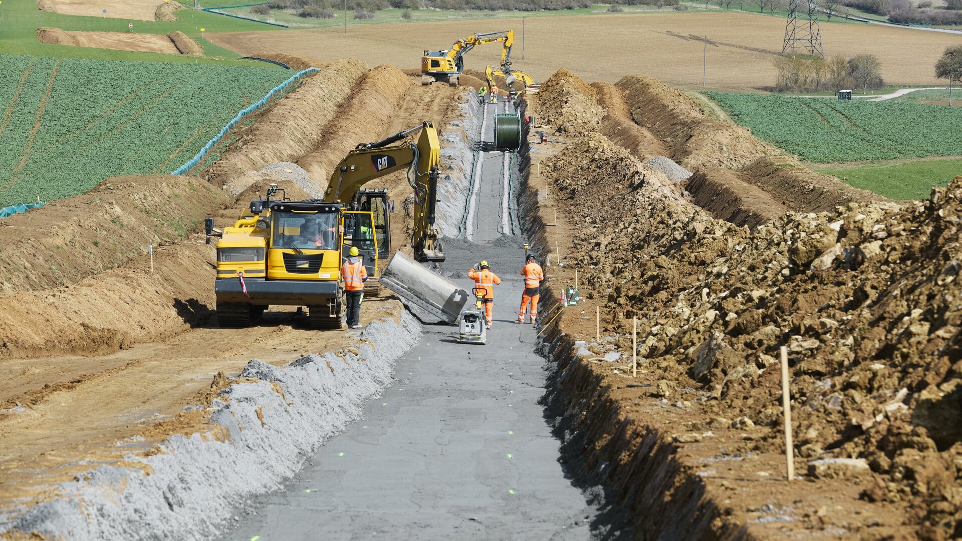 Eine Baustelle zeigt Bauarbeiter, die mit Baggern und anderen Maschinen an der Installation von Infrastruktur in ländlicher Umgebung arbeiten.