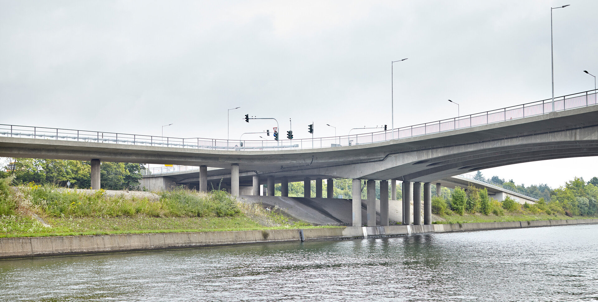 Ein Blick auf eine Brücke, die über einen Fluss führt, mit Verkehrssignalen und einer bewachsenen Uferlinie im Hintergrund.