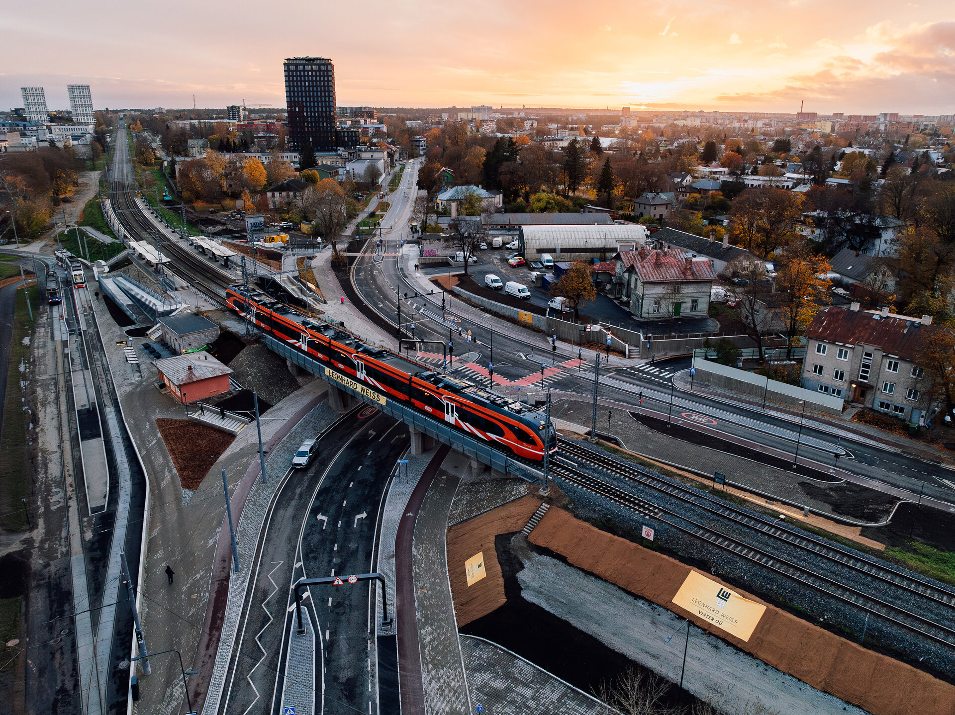 Ein Zug überquert die Kreuzung Tondi in einer urbanen Umgebung, während die Stadt Talinn im goldenen Licht der Dämmerung erstrahlt.