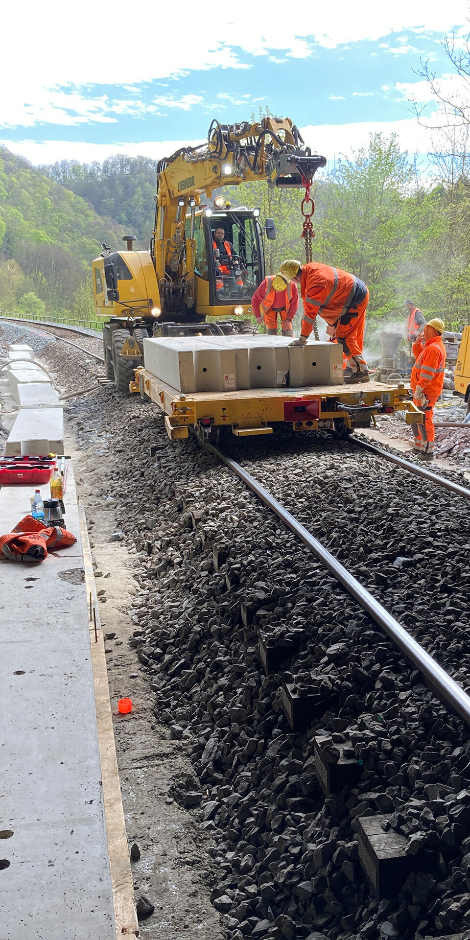 Im Tunnel sind mehrere Bauarbeiter beschäftigt, während ein Kran eine Betonplatte auf die Schienen absetzt.