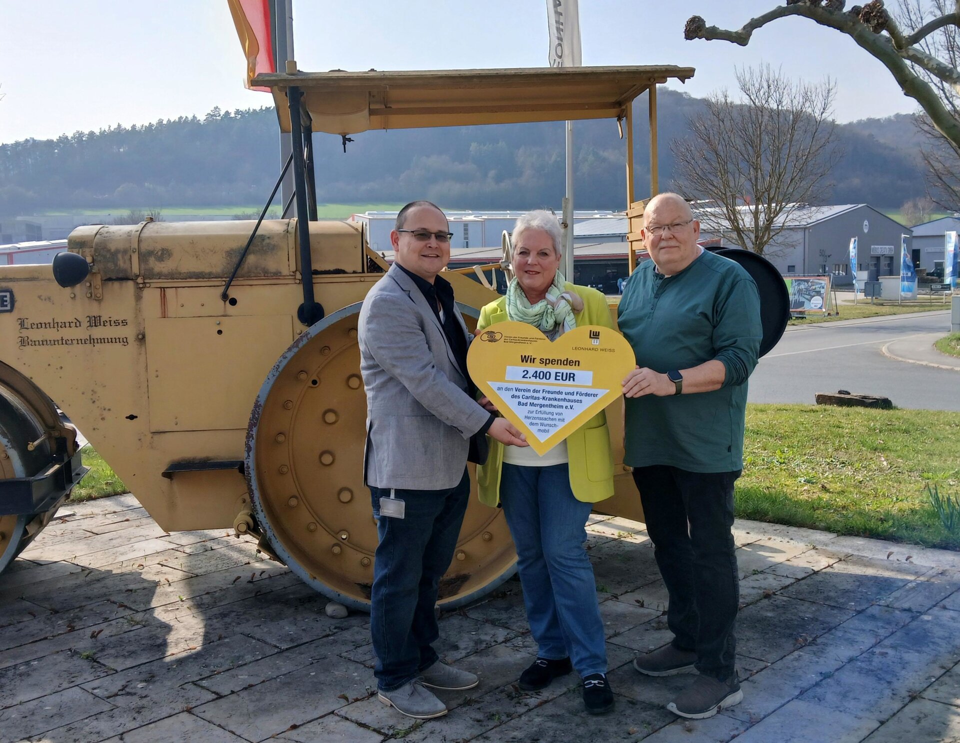 Drei Personen und ein Spendenscheck in Herzform.