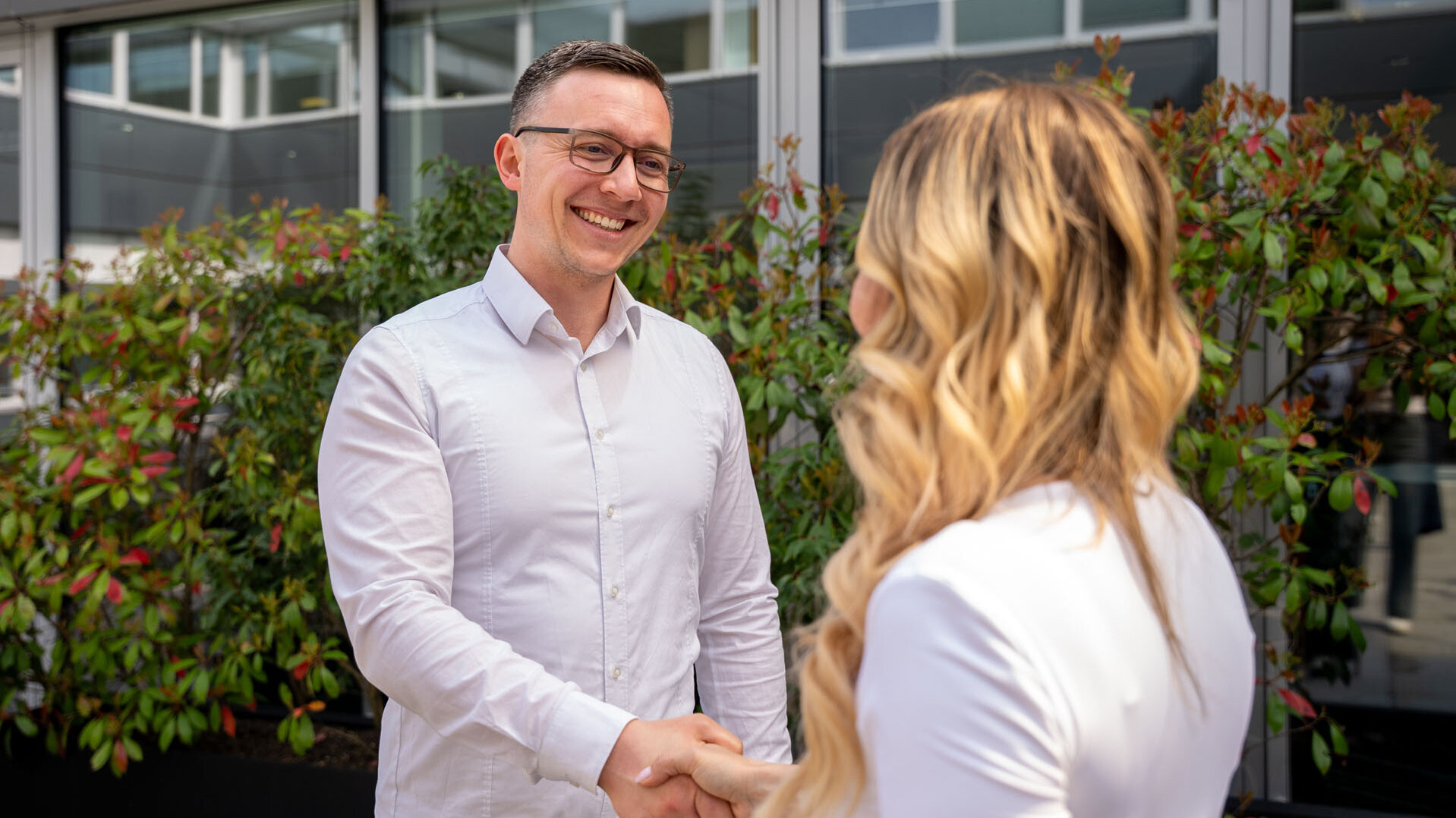Die Szene zeigt einen Mann, der einer Frau die Hand schüttelt, beide wirken freundlich und professionell in einem hellen Umfeld.