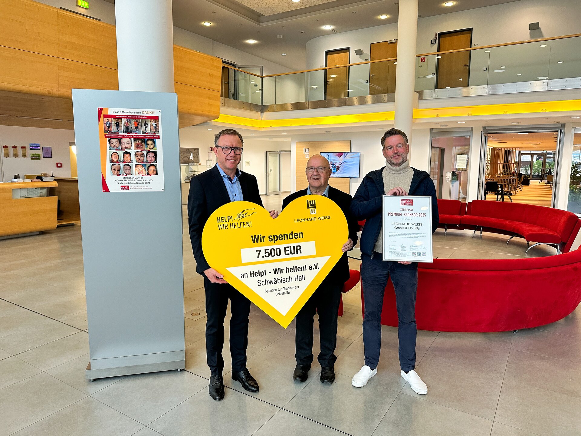 Drei Männer halten ein herzförmiges Zertifikat in einer Lobby.