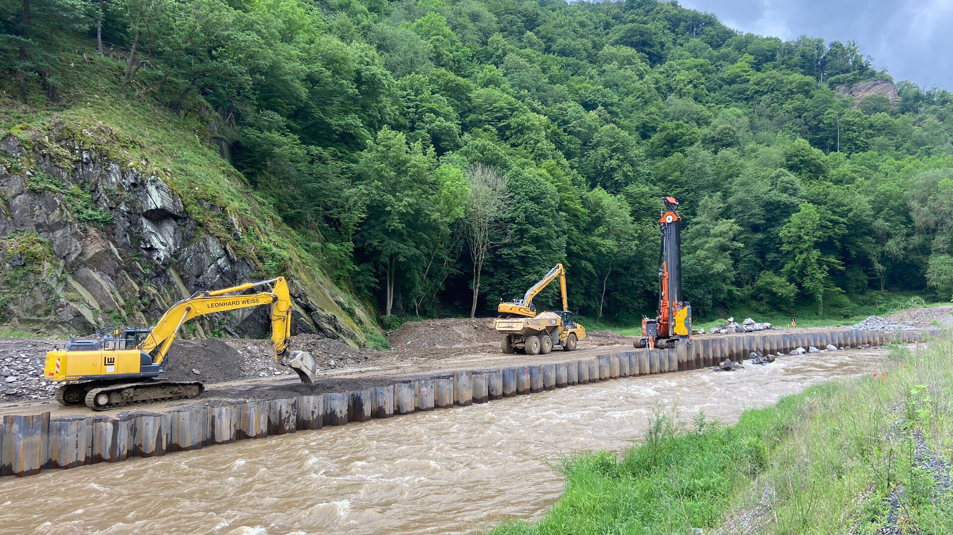 Zwei Bagger arbeiten am Ufer der Ahr, während ein Kran in der Nähe aufgestellt ist, um Bauarbeiten durchzuführen.