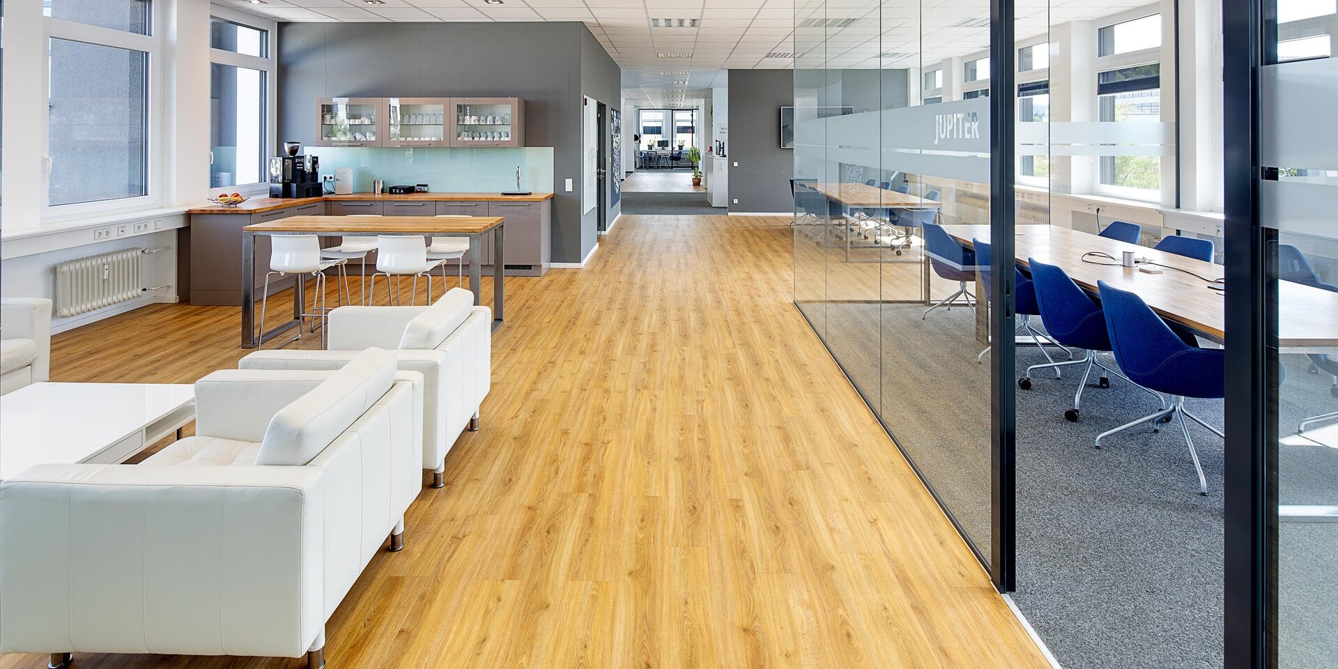 Der Raum zeigt eine elegante Mischung aus Arbeitsplätzen und einem gemütlichen Lounge-Bereich mit weißen Sofas.