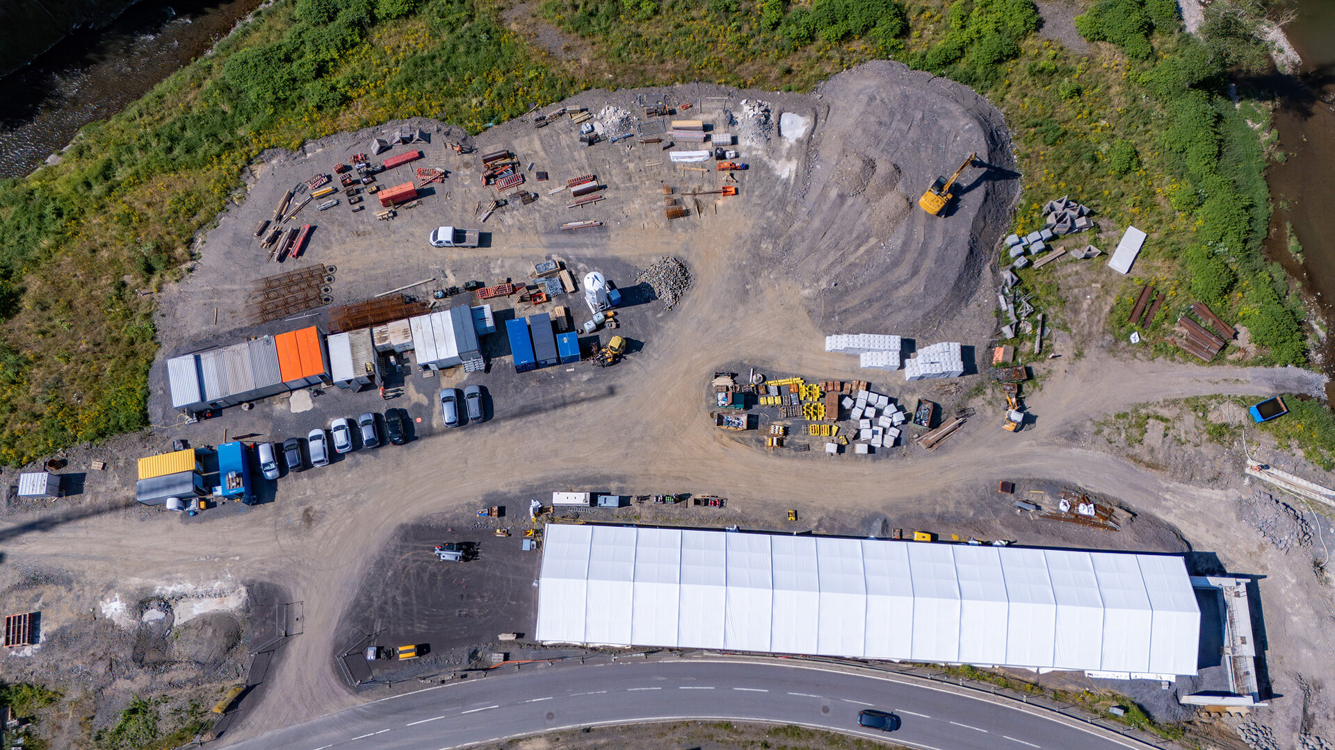 Luftaufnahme eines Baustellenbereichs mit Containern, Baumaschinen und einem großen weißen Zelt, am Ufer der Ahr.