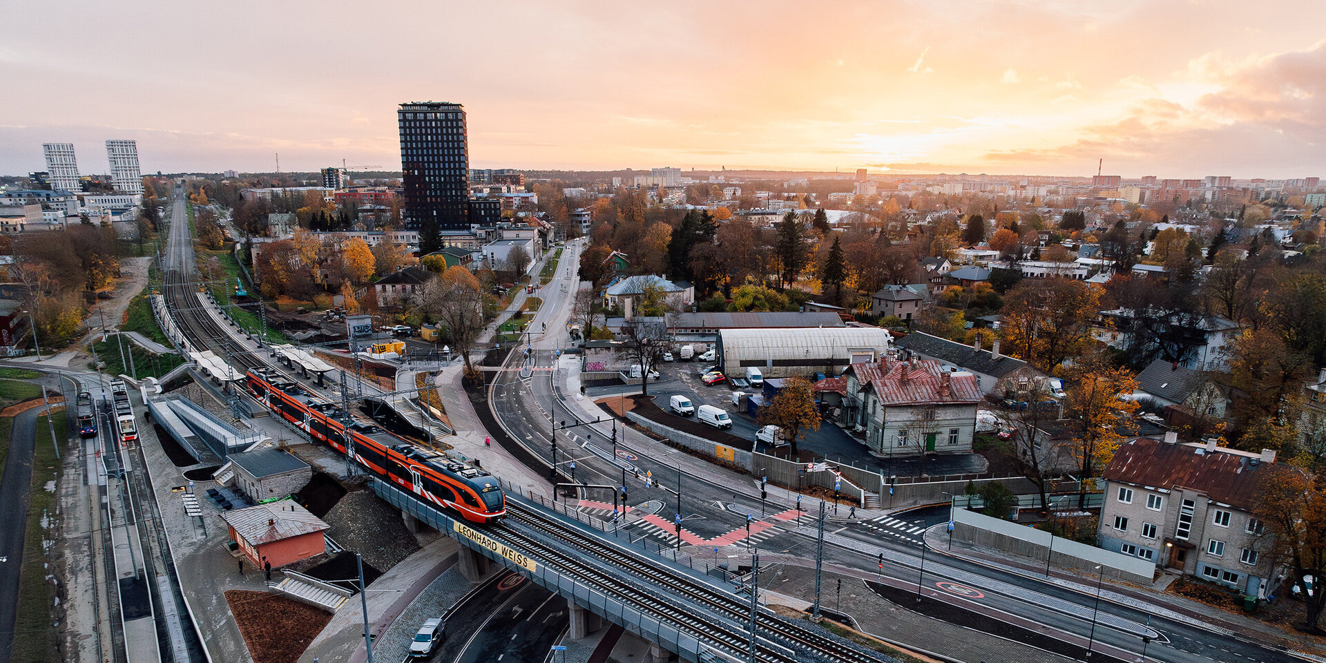 Die Szene zeigt eine belebte Stadtlandschaft mit einem Zug, der über Gleise fährt, umgeben von Straßen und Gebäuden.