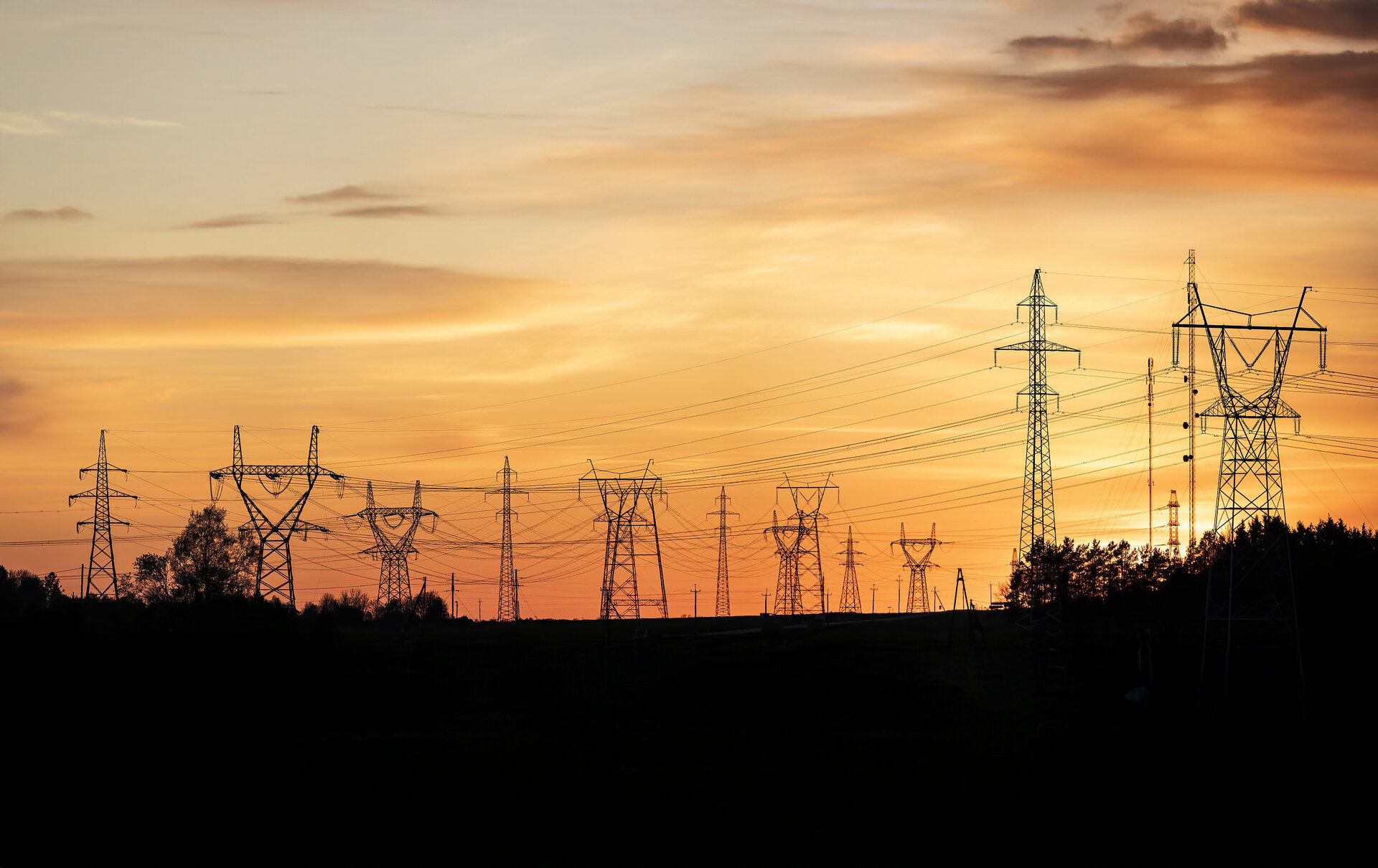 Hochspannungsleitungen erstrecken sich über die Landschaft, während die Sonne hinter dem Horizont untergeht und den Himmel erhellt.