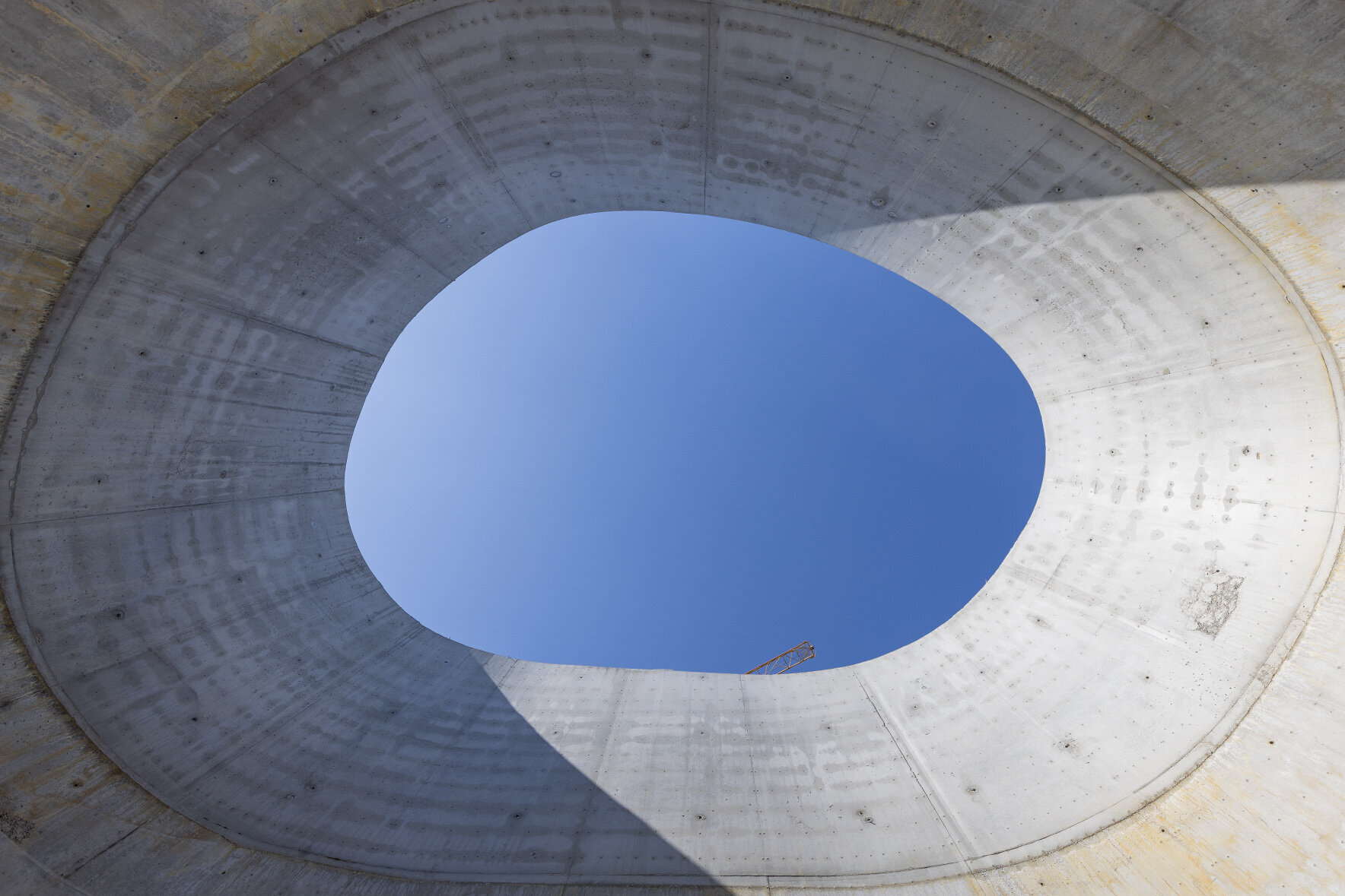 Ein Blick von unten durch eine große, ovale Tunneldeckenöffnung in den klaren blauen Himmel.