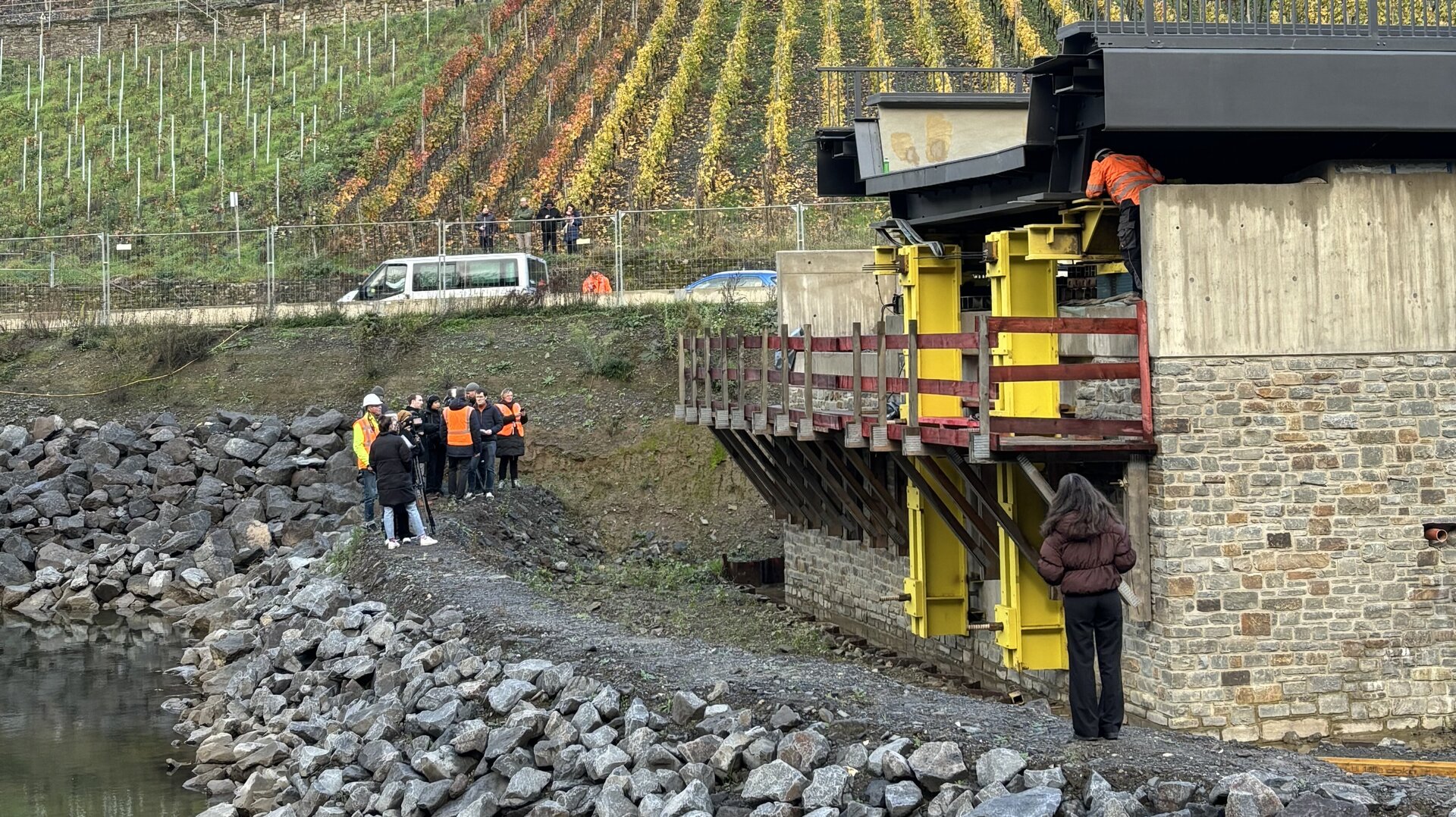 Eine Gruppe von Menschen in orangefarbenen Westen steht am Ufer der Ahr und betrachtet den Brückeneinschub zwischen der Felspartie „Bunte Kuh“ und Marienthal.