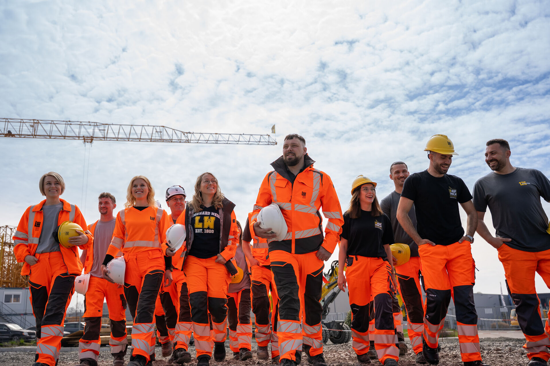 Auf einer Baustelle posiert eine Gruppe von Bauarbeitern in Sicherheitskleidung, die eine positive und motivierte Atmosphäre ausstrahlt.