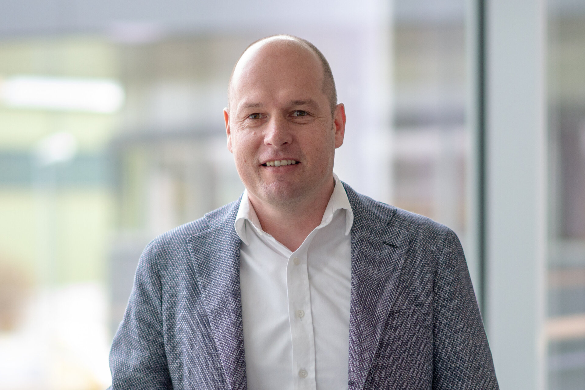 Ein Mann mit Glatze trägt ein weißes Hemd und Jackett.