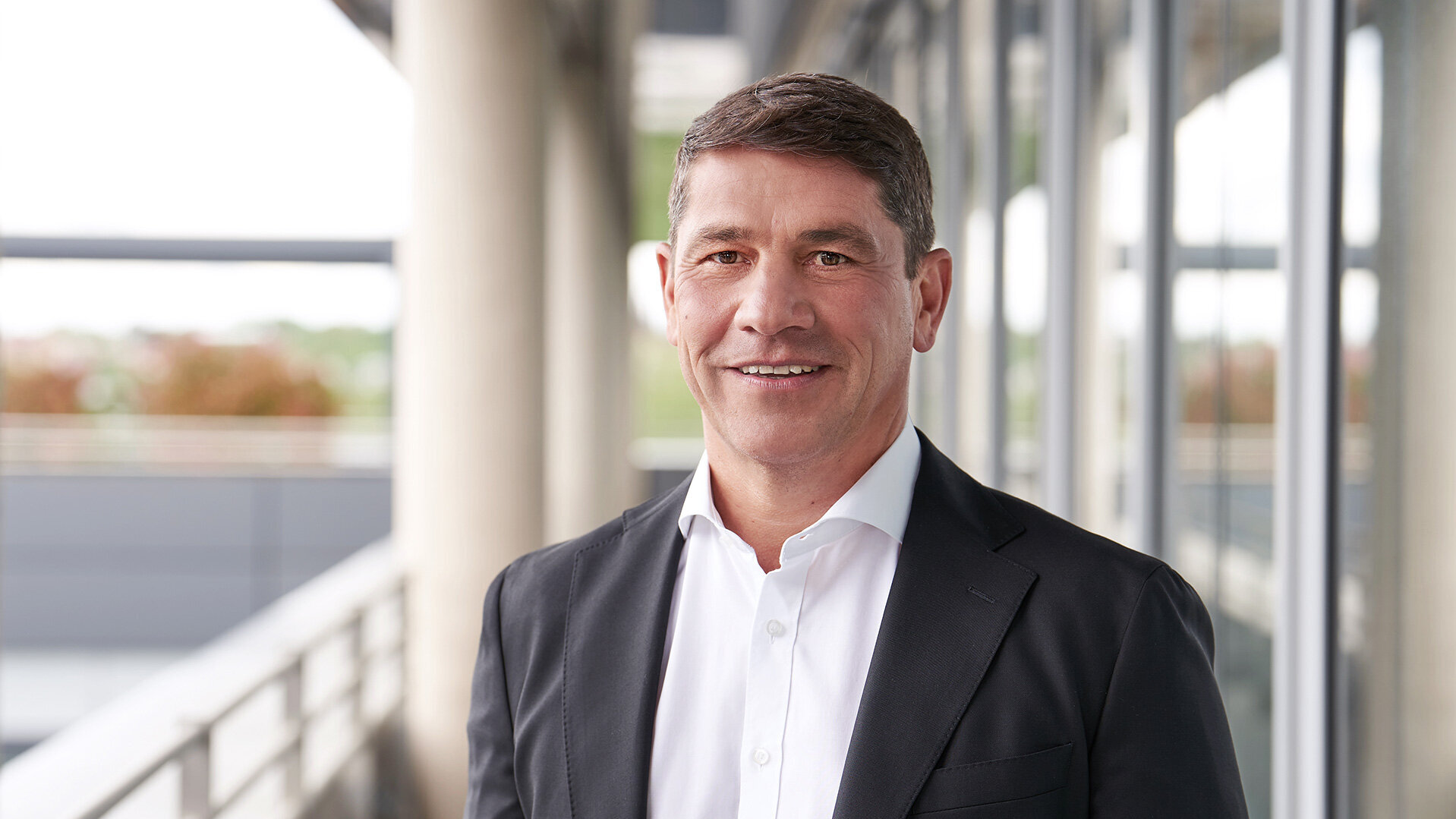 Foto von Stefan Schmidt-Weiss, Ressortleiter Ressourcen und Beteiligungen, stehend in Anzug und Hemd vor einem modernen Bürogebäude.