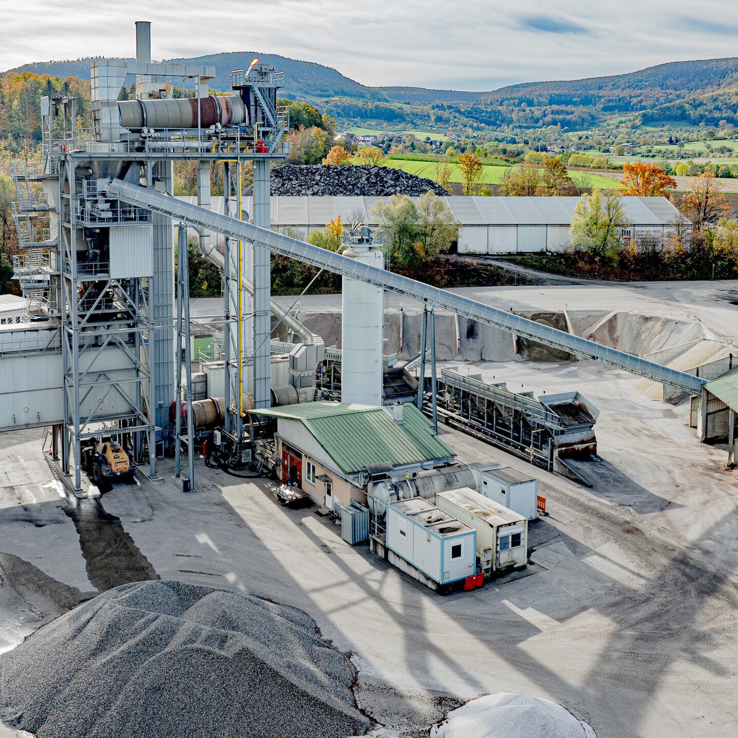 Eine große industrielle Anlage zur Materialverarbeitung, umgeben von herbstlichen Bäumen und sanften Hügeln im Hintergrund.