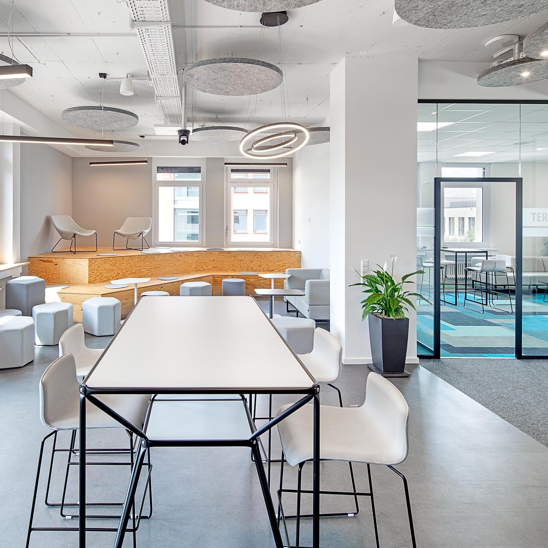 Ein moderner Büroraum mit großen Fenstern, hellen Möbeln und einer gemütlichen Sitzecke auf einer Holzplattform.