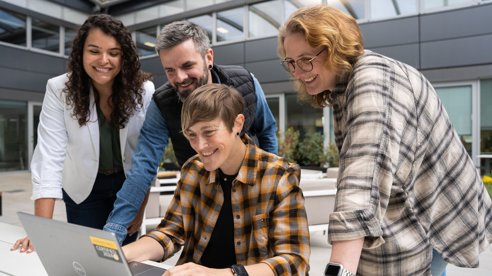 Vier Personen stehen um einen Tisch und schauen auf einen Laptop, während sie gemeinsam an einem Projekt arbeiten.