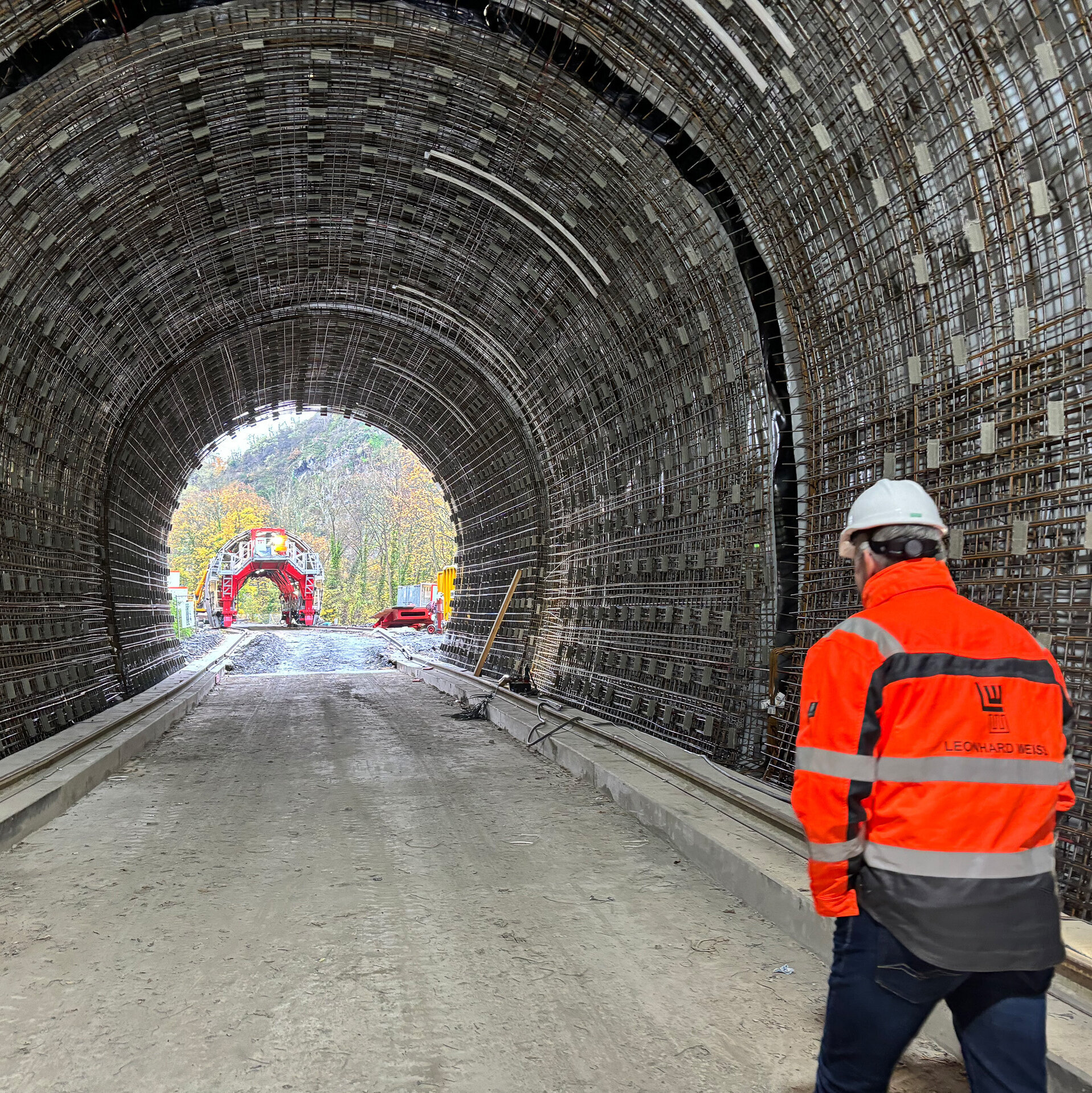 Ein Bauarbeiter in orangefarbener Sicherheitskleidung geht durch einen Tunnel, der mit Stahlgerüsten ausgekleidet ist.