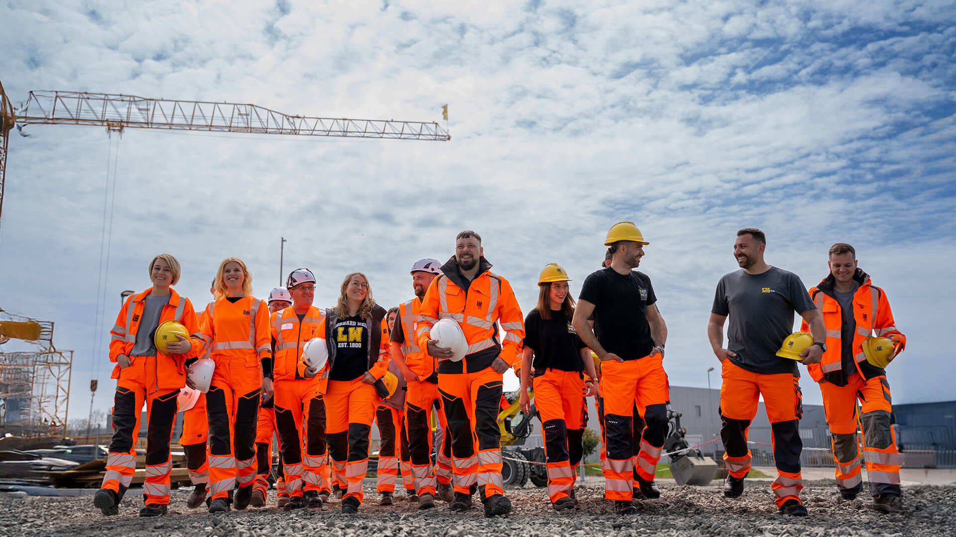 Eine gemischte Gruppe von Bauarbeitern in Sicherheitskleidung zeigt Teamgeist, während sie in einer sonnigen Umgebung zusammenarbeiten.