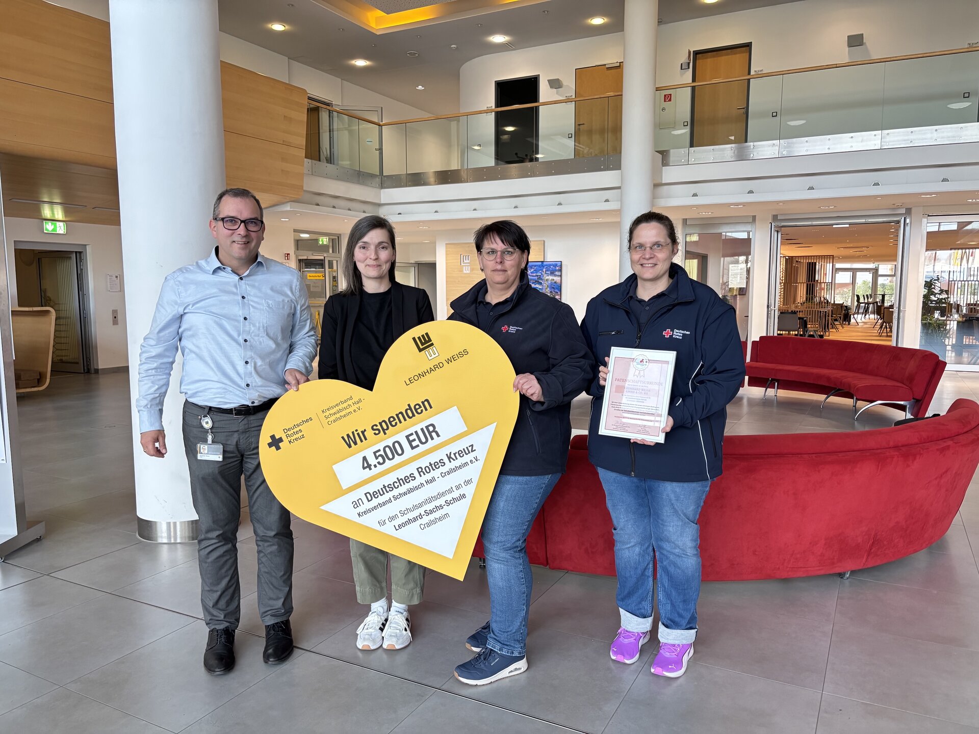 Drei Personen halten ein herzförmiges Zertifikat in einer Lobby.