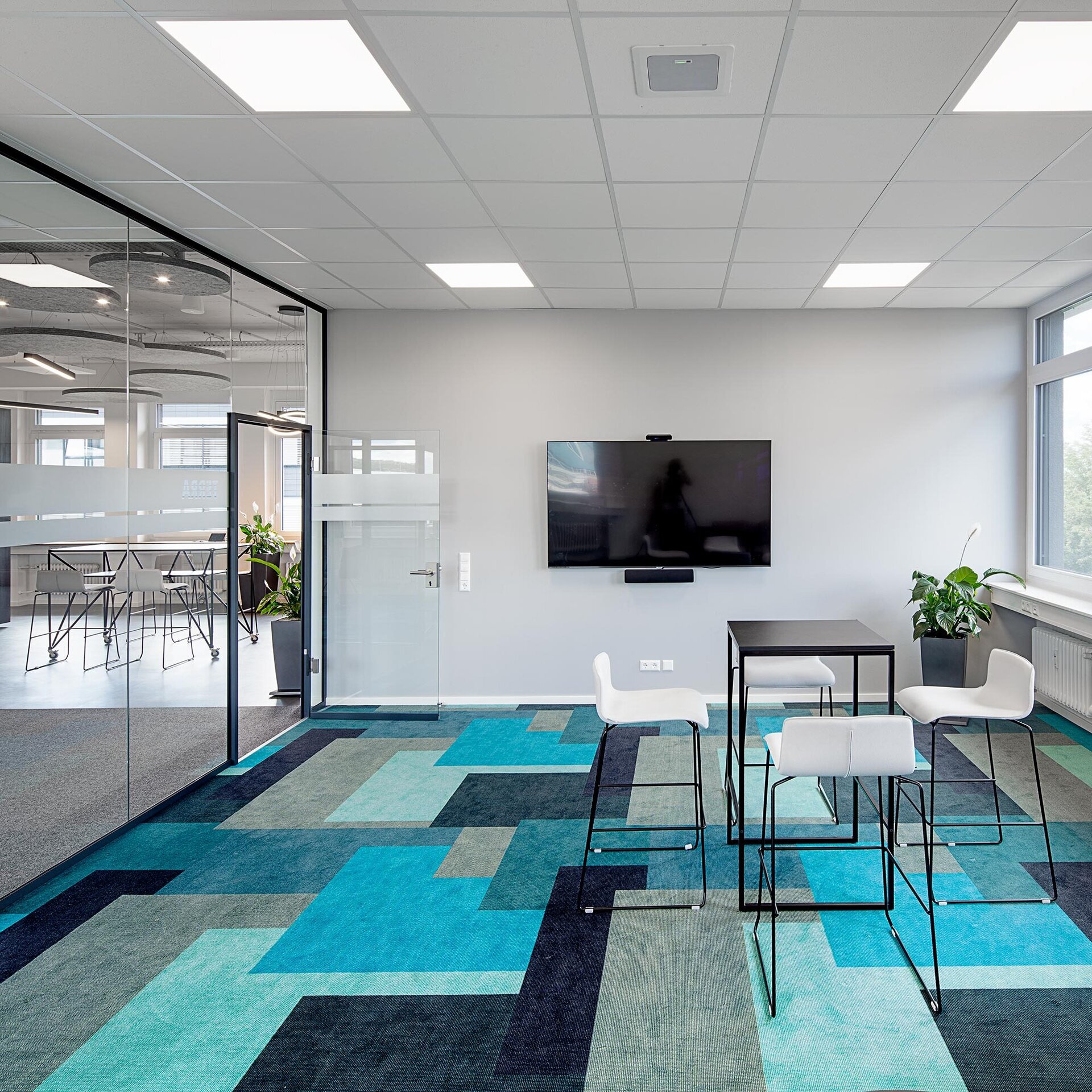 Ein moderner Büroraum mit einem stilvollen Teppich in Blau- und Grüntönen, einem Tisch und weißen Stühlen für Besprechungen.