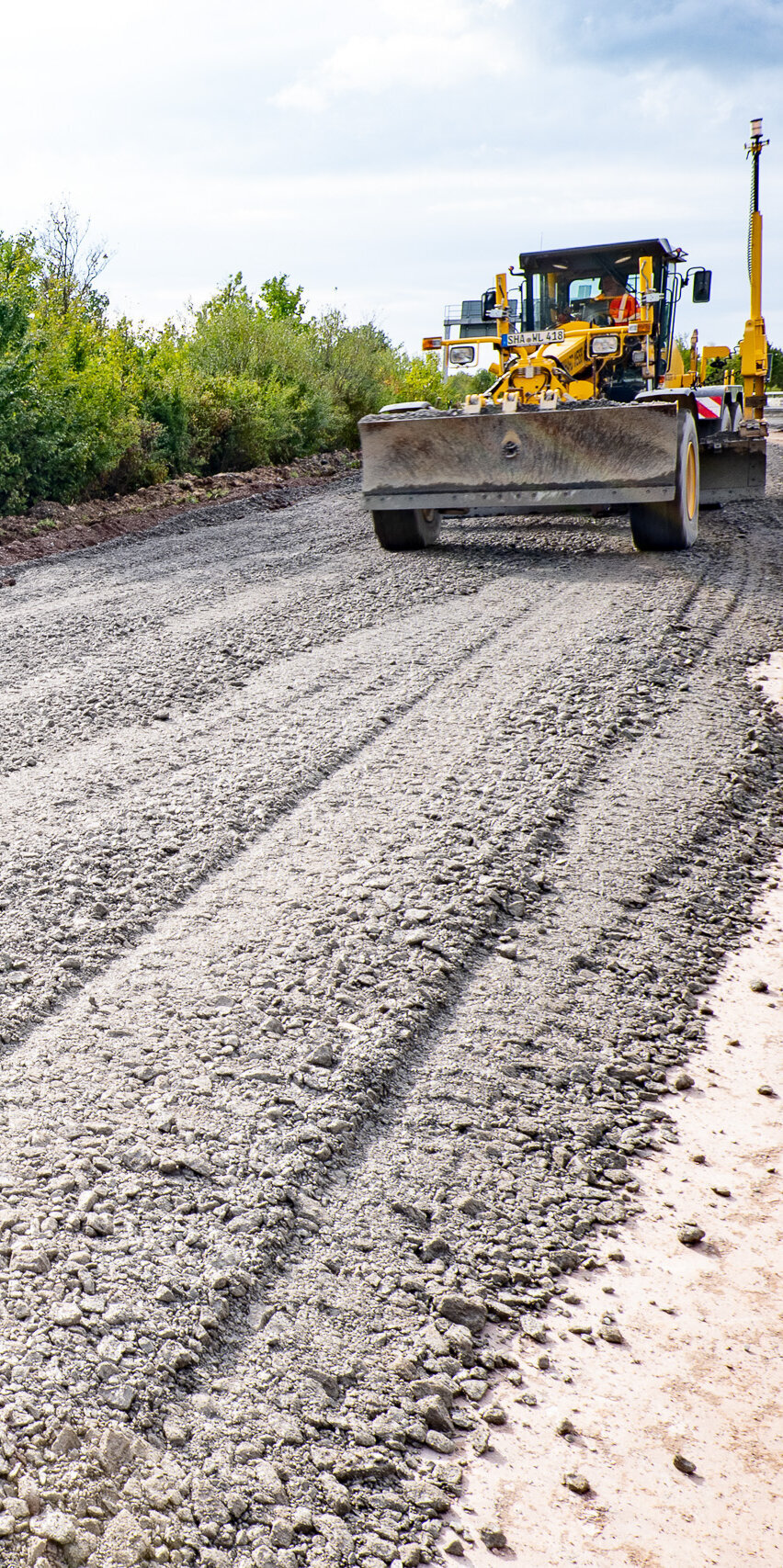 Die Baustelle zeigt eine frisch bearbeitete Straße, die von einem großen Maschinenfahrzeug geebnet wird, um eine glatte Oberfläche zu schaffen.