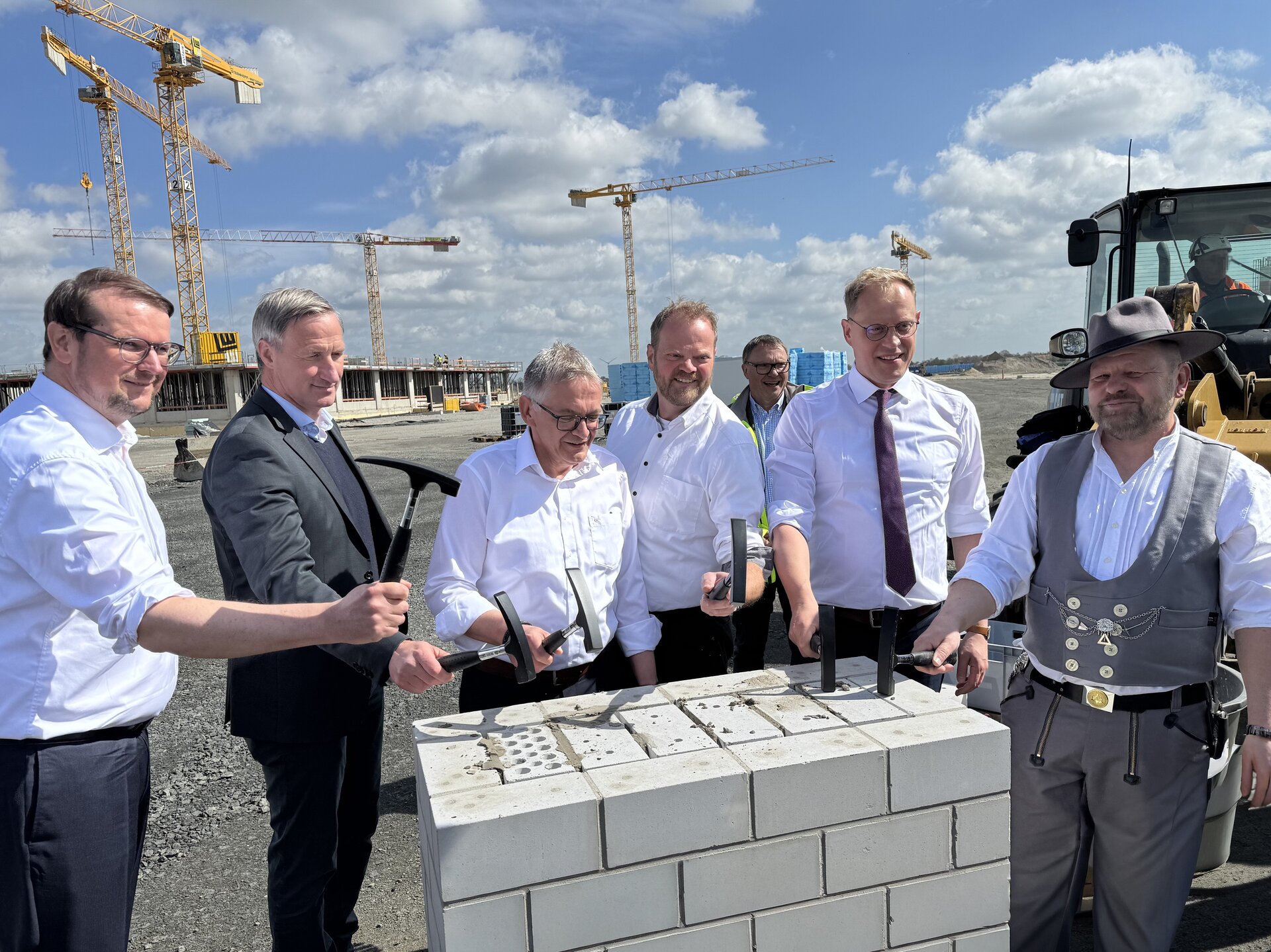 Sechs Männer stehen vor einer Mauer und haben Werkzeug in den Händen.