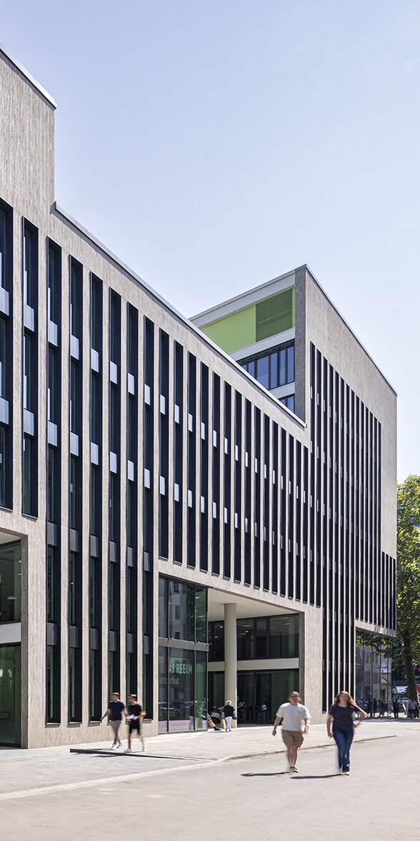 Ein elegantes Gebäude mit einer Fassade aus Glas und Beton, das von Passanten und Radfahrern frequentiert wird.