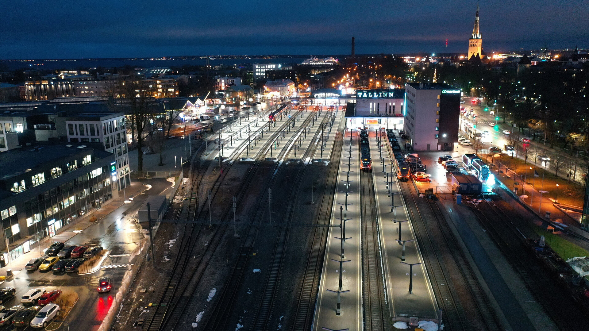 Eine nächtliche Ansicht des Bahnhofs in Tallinn, beleuchtet von Straßenlaternen und umgeben von modernen Gebäuden.