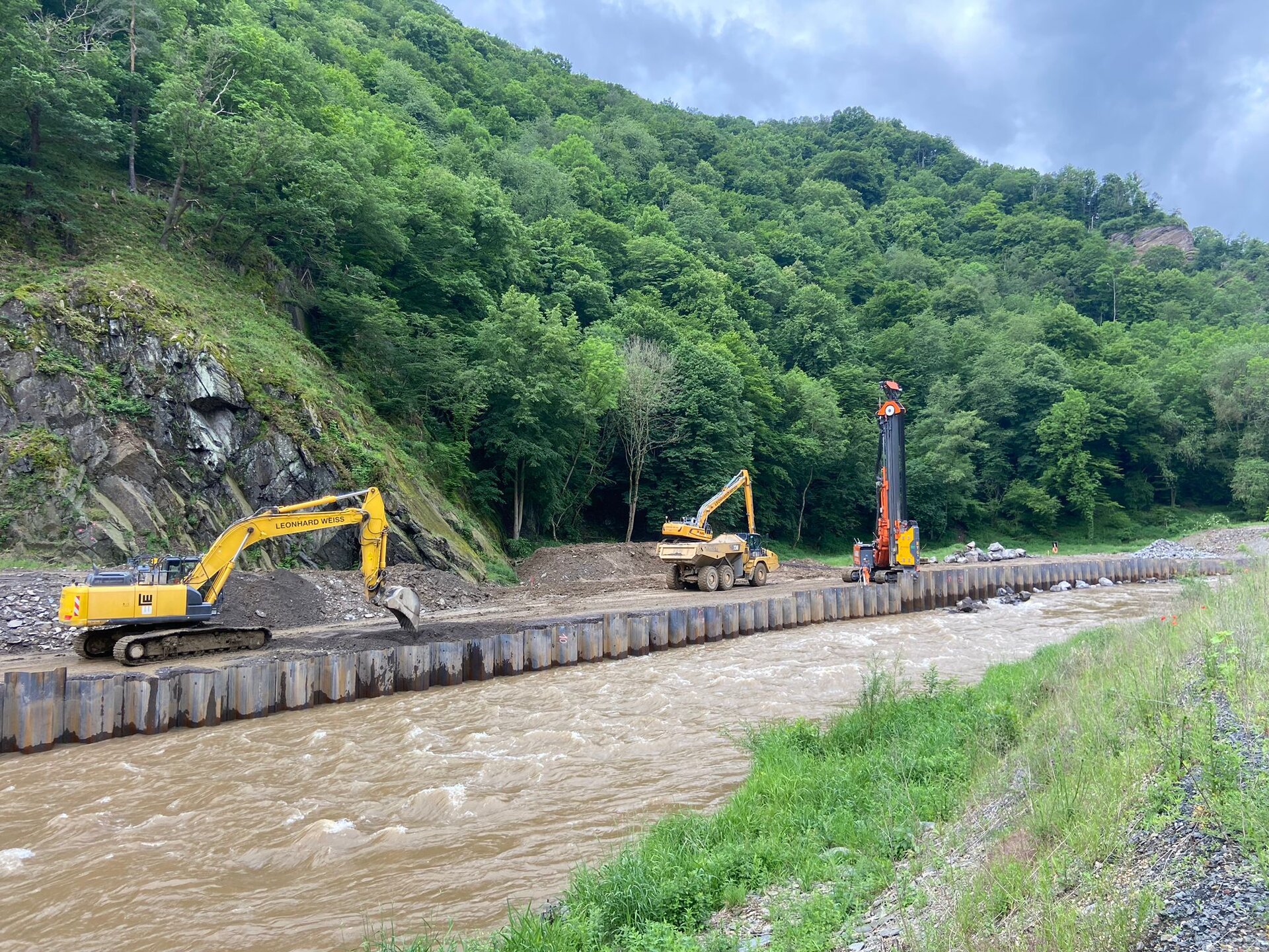 Zwei Bagger arbeiten am Ufer der Ahr, während ein Kran in der Nähe aufgestellt ist, um Bauarbeiten durchzuführen.