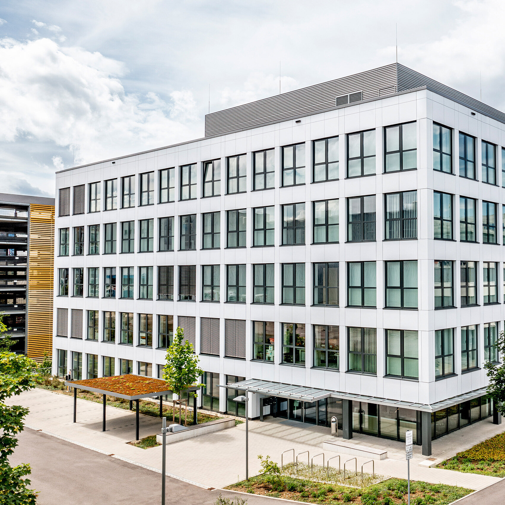Eine Ansicht eines stilvollen, modernen Bürogebäudes, das von einer gepflegten Umgebung mit Bäumen und Parkplätzen umgeben ist.
